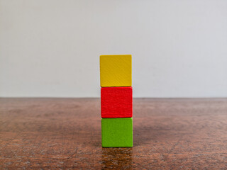 Stack of three vibrant wooden blocks in yellow, red, and green colors arranged vertically on a polished wooden table against a plain background.