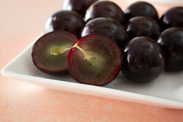 A closeup view of a plate of muscadine grapes, featuring one that is halved.