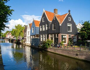 Obraz premium Charming canal-side houses in a Dutch town, reflecting in the tranquil water under a sunny sky.