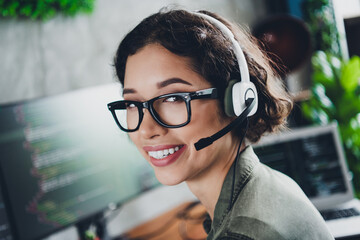 Smiling female programmer wearing a headset working on computer in a modern office setting,...