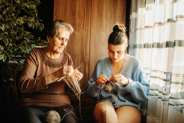 Senior caucasian woman teach granddaughter how to knit with needles