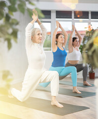 Elderly woman practicing yoga poses with other women in yoga studio