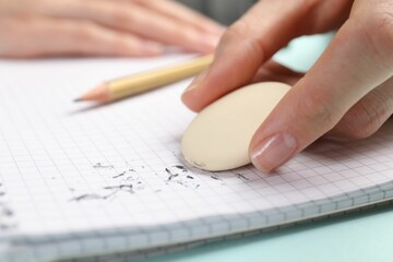 Woman rubbing eraser against paper at light blue table, closeup