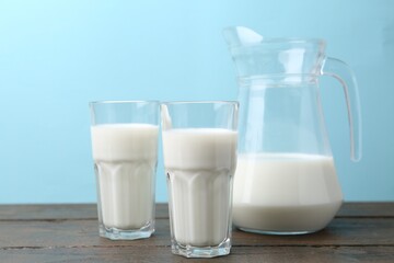 Fresh milk on wooden table against light blue background