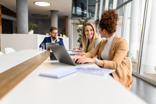 Smiling businesswoman discussing ideas with female colleague working on laptop in collaborative office - Powered by Adobe