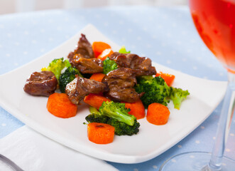 Roasted chicken hearts served with colorful garnish of green broccoli and orange carrots on white dish..