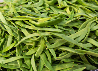 Many of young bean pods at market for sale. Green vegetable background.