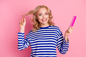 Smiling Woman in Casual Blue Striped Pullover Holding Pink Comb Against a Bright Pink Background....