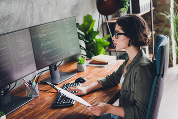 Young female programmer working on computer in modern workspace focusing on coding tasks with dual monitors and casual style
