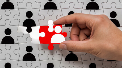 A close-up photograph of a hand placing a red and white jigsaw puzzle piece into a puzzle pattern.