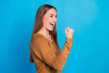 Happy young woman celebrating success while wearing a cozy sweater against a vibrant blue...