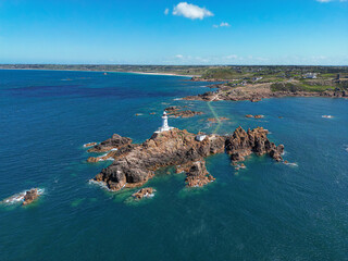 Scenic aerial drone view of La Corbiere lighthouse on a rocky island surrounded by the blue sea. Jersey, Channel Islands