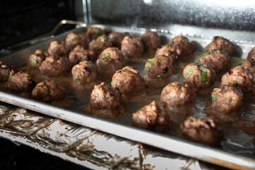 A view of a baking sheet of cranberry meatballs in the oven.