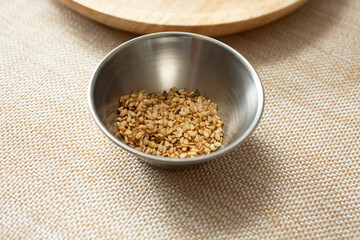 A closeup view of a metal condiment cup of roasted sesame seeds.