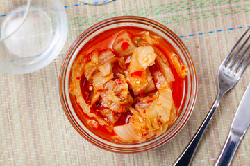 Kimchi cabbage in a bowl with chopsticks for eating on wooden background, top view, Korean food