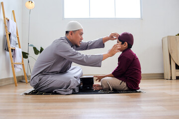 Fototapeta premium Side View Of Father Tidying Son Before Learning Holy Book Or Al Qur'an At Home