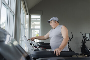 Fat man chooses running program on treadmill in gym