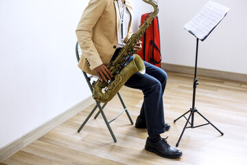 Naklejka premium Cropped Shot Of Jazz Musician Hands Playing Saxophone While Sitting On Chair
