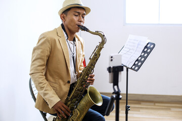 Portrait Of Young Asian Male In Formal Suit Playing Saxophone While Doing Live On Social Media