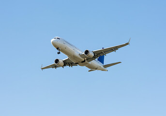 A white airplane with blue tail flying in a clear blue sky on a sunny day with landing gear down ready
