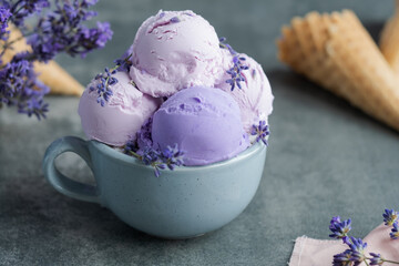 Close up creamy lavender ice cream on a mug, decorated with lavender flowers on a gray background. Healthy dessert frozen. Sweet vegan breakfast