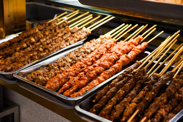 Grilled meat skewers on metal trays at a street food stall in Shanghai, China. Various spices and marinades create a colorful display