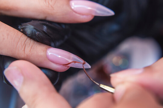 Close-up of a beauty technician using a fine detailing brush to paint intricate gel polish designs on shaped extensions during a nail art session.