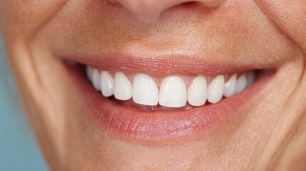 Woman mouth smiling. Her teeth are white and healthy, and she has a gentle smile on her face. The image is likely taken indoors, as the background is a plain blue, cropped.