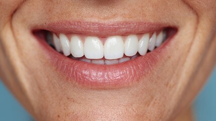 Woman mouth smiling. Her teeth are white and healthy, and she has a gentle smile on her face. The image is likely taken indoors, as the background is a plain blue, cropped.