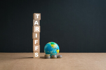 Tariffs, word on square wooden blocks, next to planet globe and coins. 