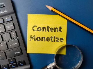 Black keyboard and magnifying glass with the word Content Monetize on a yellow sticky note