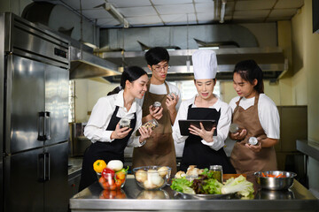 Smiling chef teacher using a tablet to explain a recipe to students in a professional kitchen