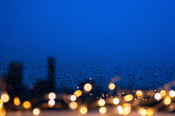 Raindrops on glass window with golden lights and blurred city background.