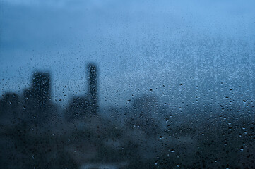 Raindrops on glass with soft city silhouette background.