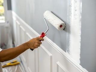 Hispanic man painting a wall during home renovation with paint roller in hand near open window and door. Concept of anti mold paint, DIY, decoration