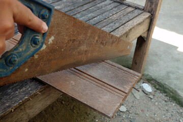 Hand holding saw while cutting a piece of wood on a rustic outdoor table