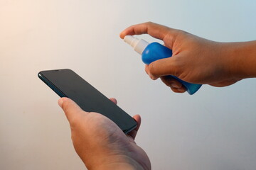 Hands using a blue spray bottle to clean a smartphone screen promoting hygiene and cleanliness.