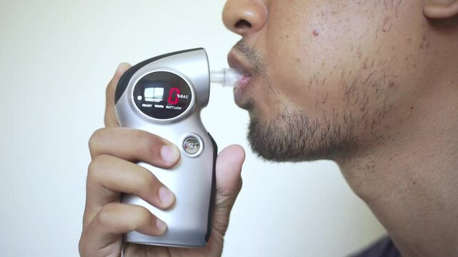 Man blows into breathalyzer to check presence of alcohol in blood and to be safe before car trip. Young guy takes breathalyzer test to prove to police that doesnt have hangover after party.