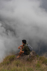 Hiker man enjoying beautiful sunrise in morning mountains. Traveler on mountain with white fog below.