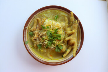 A hearty bowl of traditional Indonesian chicken soup (soto ayam) with chicken feet, bean sprouts, vermicelli, and fresh herbs.