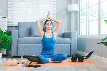 Young Asian woman practices yoga by stretching her back on a yoga mat in the living room at home....