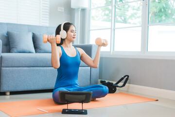 Young Asian woman practices yoga by stretching her back on a yoga mat in the living room at home....