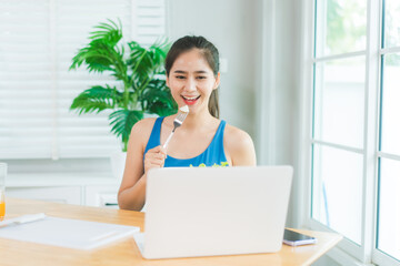 Beautiful Asian woman in fitness sportswear happily smiles while slicing vegetables and fruits on...
