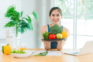 Beautiful Asian woman in fitness sportswear happily smiles while slicing vegetables and fruits on...