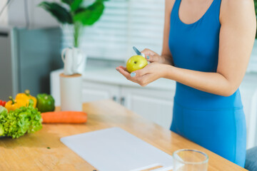 Beautiful Asian woman in fitness sportswear happily smiles while slicing vegetables and fruits on...