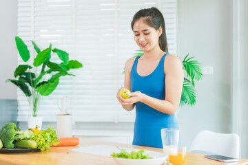 Beautiful Asian woman in fitness sportswear happily smiles while slicing vegetables and fruits on...