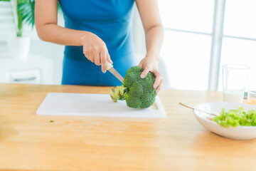 Beautiful Asian woman in fitness sportswear happily smiles while slicing vegetables and fruits on...