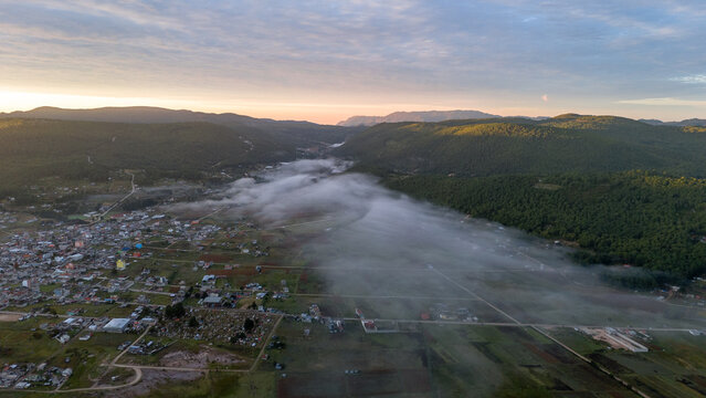 Amanecer en pueblo con nubes por debajo y un cielo azul con monta&ntilde;as de fondo y el sol saliendo peque&ntilde;o poblado chalcatongo, Oaxaca foto aerea de drone 