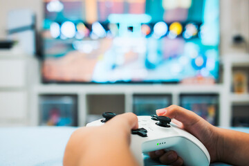 A child with a gamepad is playing in the bed room with lights around the TV on.	