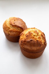 Two muffins lie on a white surface. The muffins are golden brown and have a slightly crispy texture. Homemade baking and pastry from wheat flour. Making bread and Easter cakes